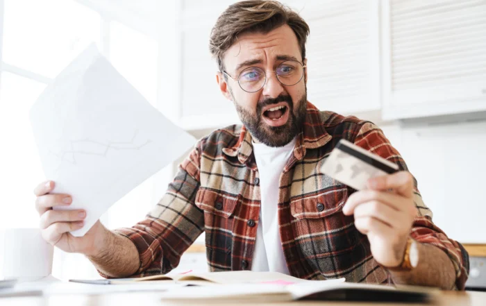 Worried man reviewing bills and financial documents while holding a credit card, illustrating the consequences of missing Chapter 13 bankruptcy payments in Louisiana.